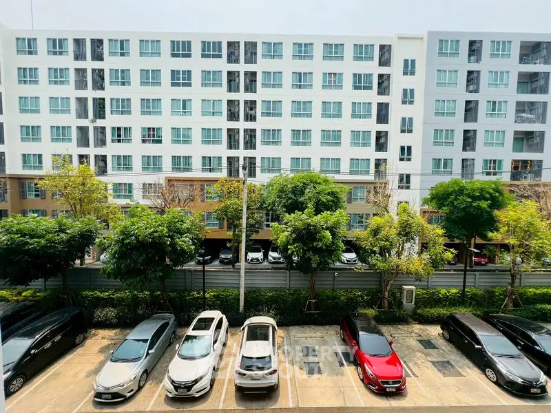 Modern apartment building with parking lot and lush greenery in urban setting.