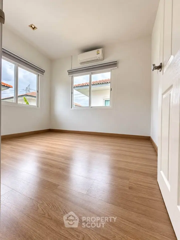 Spacious empty bedroom with wooden flooring and natural light from windows.