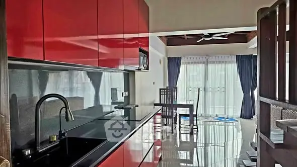 Modern kitchen with sleek red cabinets and open layout leading to dining area with natural light.
