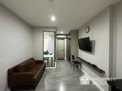 Modern minimalist living room with sleek wooden flooring, cozy brown leather sofa, and wall-mounted flat-screen TV, leading to a well-lit corridor.