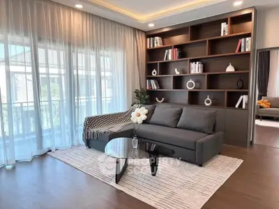 Elegant living room with modern sofa, glass coffee table, and built-in bookshelf, featuring large windows and natural light.