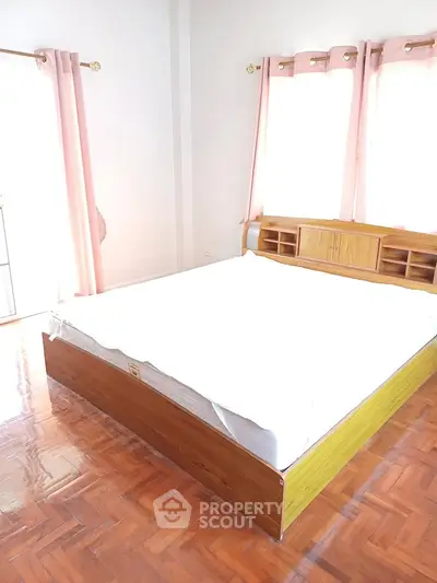Spacious bedroom with natural light and wooden flooring, featuring a large bed and elegant curtains.