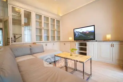 Elegant living room with modern sectional sofa and built-in cabinetry, featuring a flat-screen TV and ambient lighting.