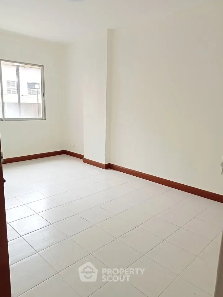 Spacious empty room with white tiled floor and large window, perfect for customization.