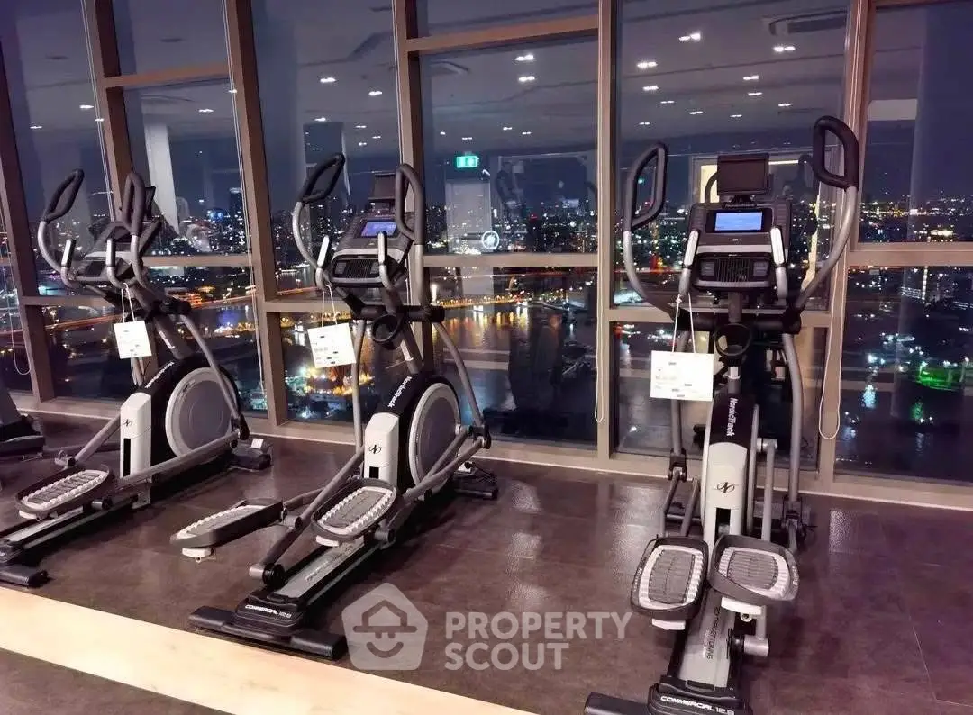 Luxurious gym with modern equipment and stunning city view from large windows.