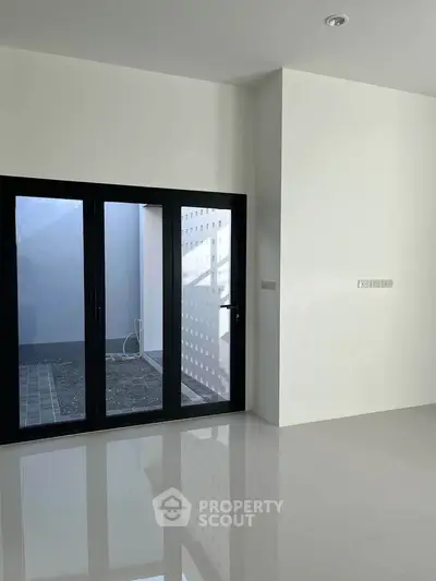Modern minimalist interior with sleek sliding glass doors and polished floors, leading to a small outdoor area.