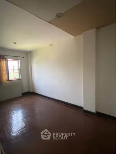 Spacious empty room with wooden flooring and natural light from window.