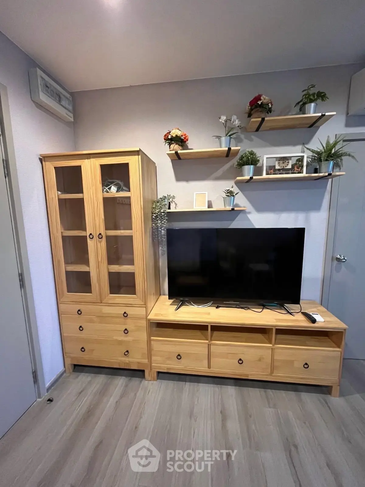 Modern living room with wooden furniture and TV, featuring stylish shelves and decor.