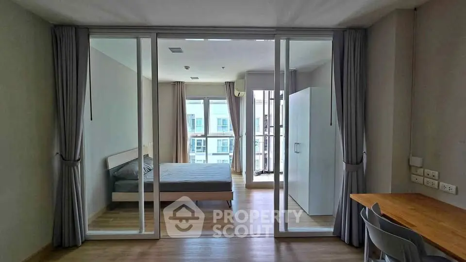 Modern bedroom with glass partition, wooden flooring, and ample natural light in a stylish apartment.