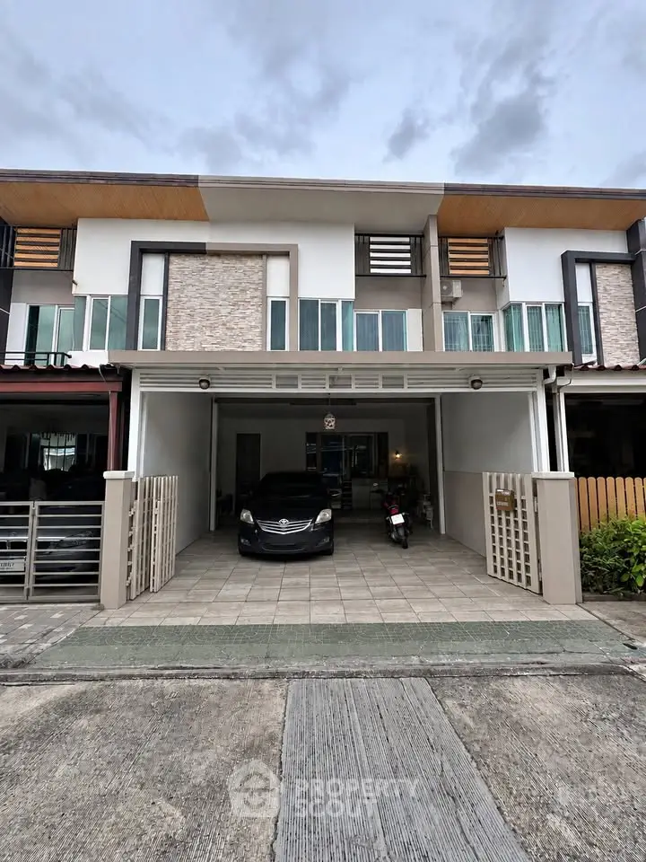 Modern townhouse exterior with garage and parked vehicles, showcasing contemporary design and urban living.