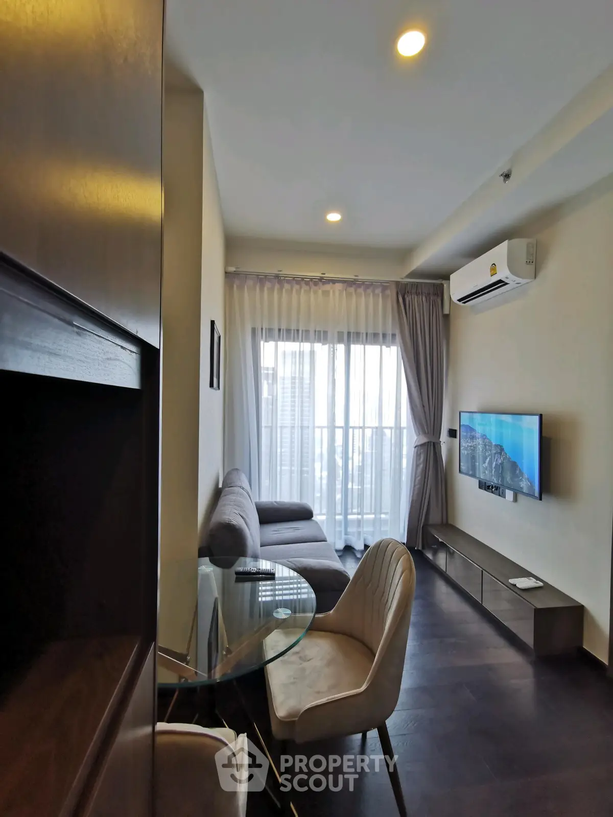 Modern living room with sleek furniture and large window offering city views.