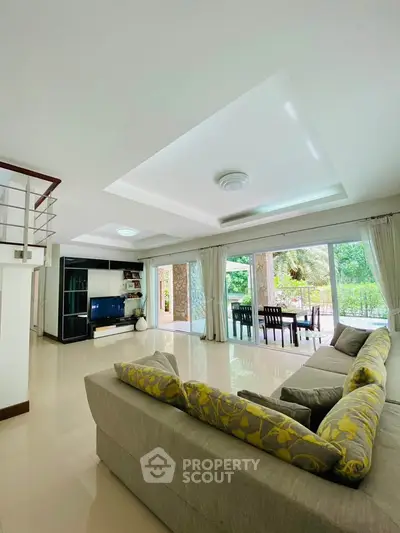 Spacious living room with modern decor and large windows overlooking lush greenery.