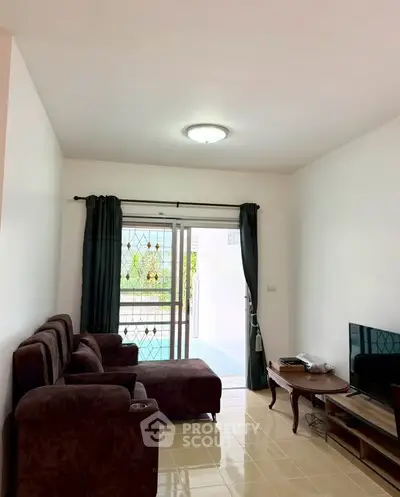 Cozy living room with plush seating and TV, opening to a bright balcony view.