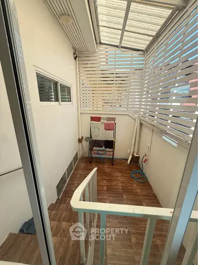 Charming enclosed balcony with wooden flooring and ample natural light, perfect for relaxation or utility use.