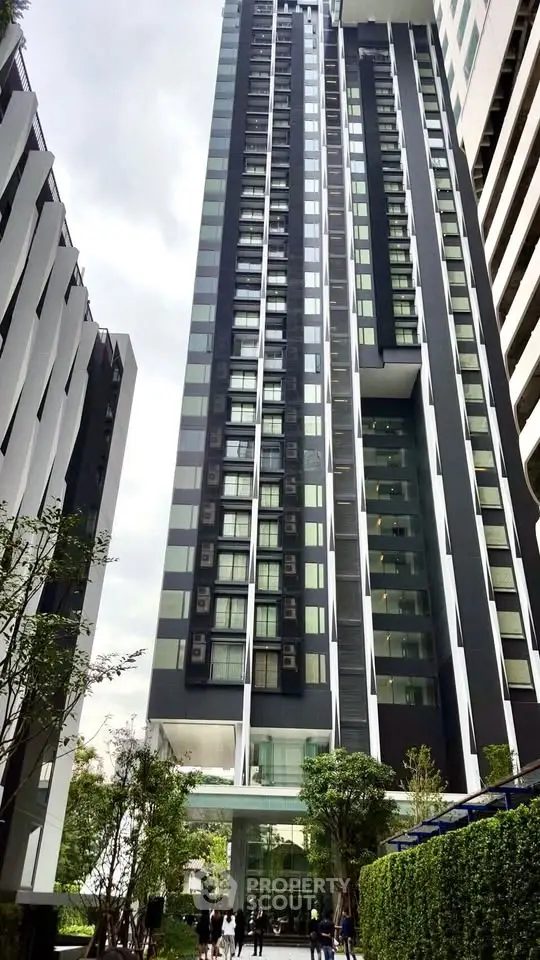 Modern high-rise building with sleek design and lush greenery at the entrance.