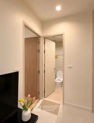 Modern apartment interior with hallway leading to a bathroom, featuring sleek design and neutral tones.