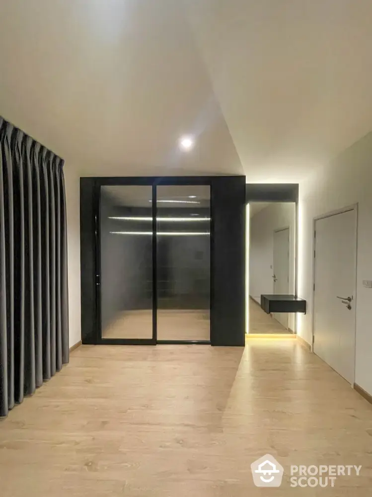 Spacious and modern living area with sleek black sliding doors leading to a well-lit room, featuring warm wooden flooring and minimalist design.