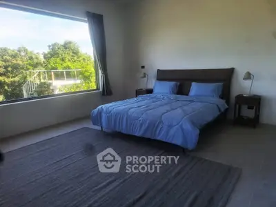 Spacious bedroom with large window offering lush green views, modern decor, and cozy ambiance.