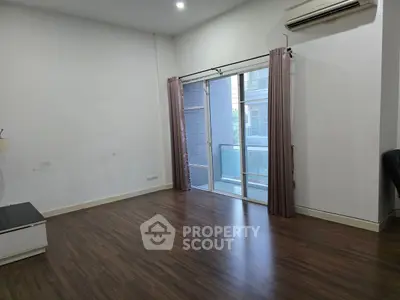 Spacious empty room with wooden flooring and large window for natural light.