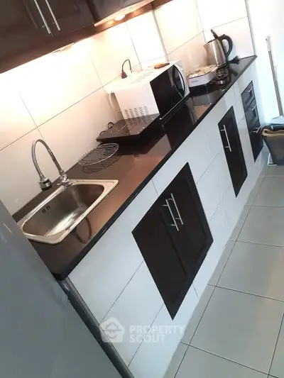 Modern kitchen with sleek cabinets, microwave, and kettle on a black countertop.