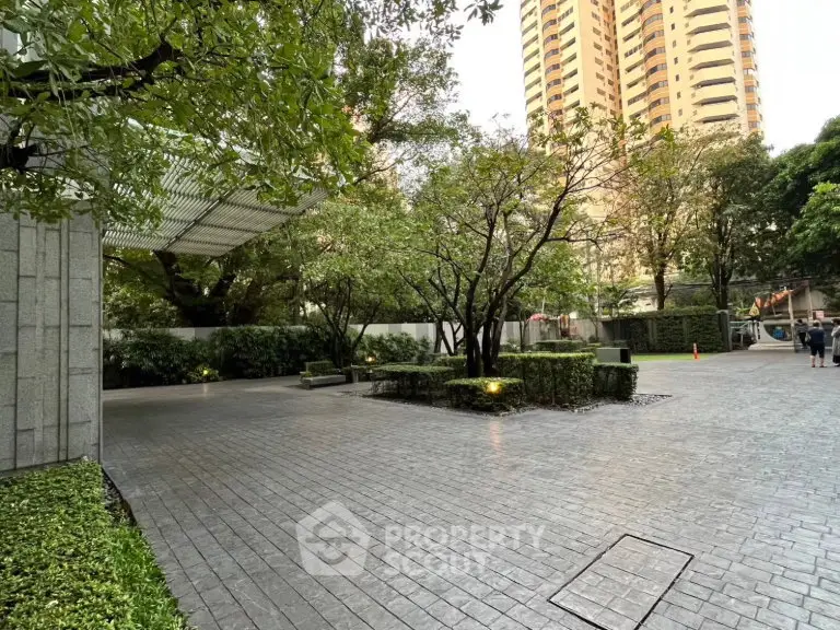 Elegant building entrance with lush greenery and paved walkway in a serene urban setting.