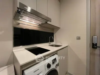 Compact modern kitchen with washing machine and induction cooktop in sleek apartment.