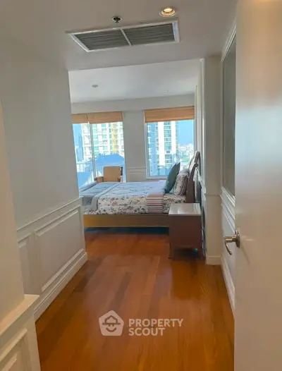 Spacious bedroom with wooden flooring and large windows offering city views in a modern apartment.