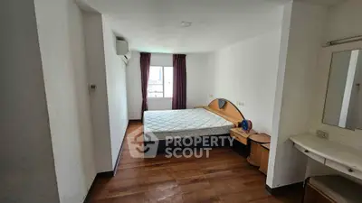 Spacious bedroom with wooden flooring and large window offering natural light.