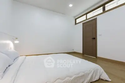 Minimalist bedroom with white walls and bedding, featuring a wooden door and floor.