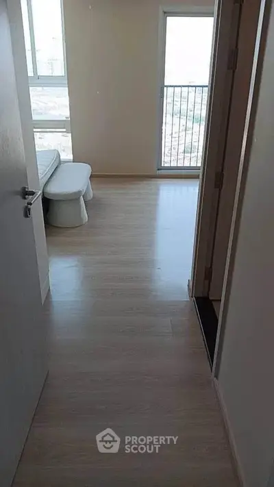 Bright hallway leading to a bedroom with a view, featuring modern flooring and natural light.