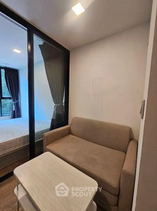 Cozy living room with a compact sofa and glass partition leading to a bedroom, perfect for modern living.