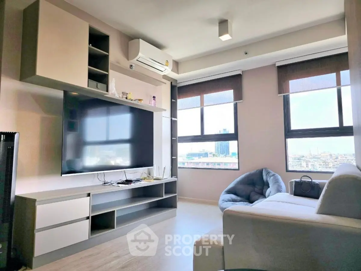 Modern living room with large TV and city view, featuring stylish furniture and natural light.