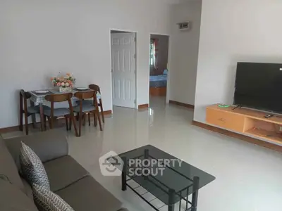 Spacious living room with modern furniture and TV, leading to a cozy bedroom.