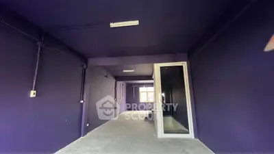 Spacious industrial-style room with dark walls and large window, ideal for creative workspace or studio.