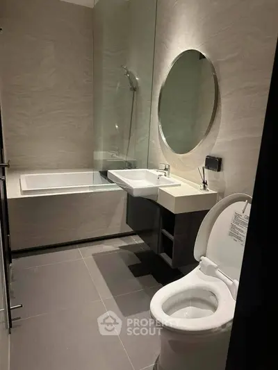 Modern bathroom with sleek design featuring a bathtub, round mirror, and contemporary fixtures.