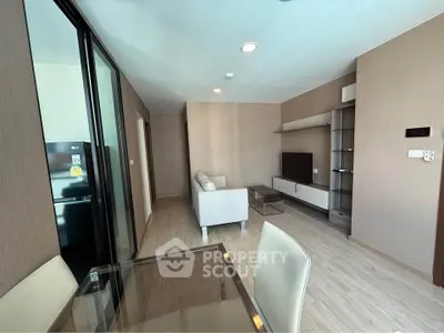 Modern living room with sleek furniture and open layout, featuring a glass dining table and flat-screen TV.