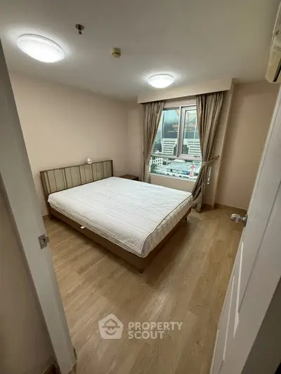 Cozy bedroom with wooden flooring and large window offering natural light