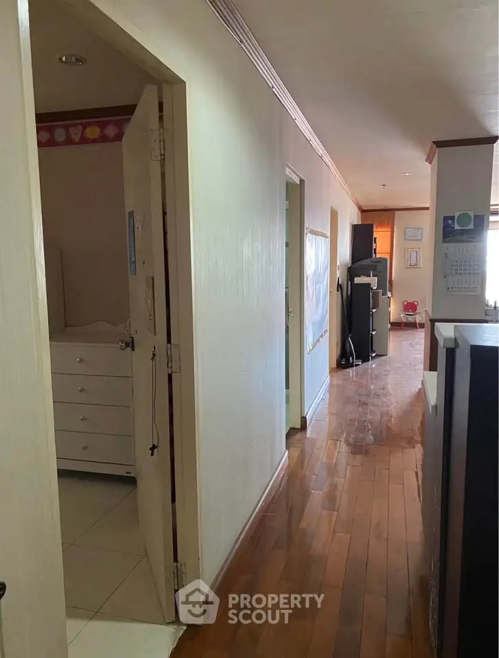 Spacious hallway with wooden flooring leading to multiple rooms in a well-lit apartment.