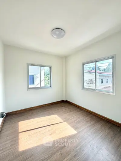 Bright empty room with wooden flooring and large windows offering natural light and views.