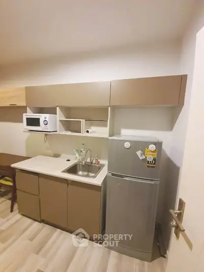 Modern compact kitchen with sleek cabinetry and stainless steel fridge in cozy apartment.