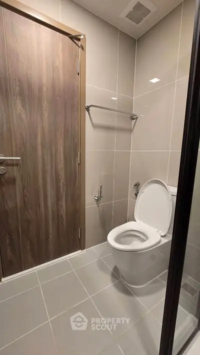 Modern bathroom with sleek design and neutral tones, featuring a toilet and wooden door.