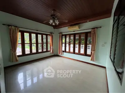 Spacious living room with large windows and ceiling fan, perfect for natural light and ventilation.