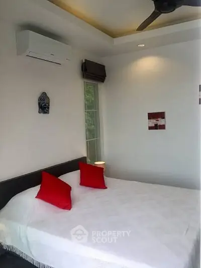 Cozy bedroom with modern decor and red accents, featuring air conditioning and natural light.