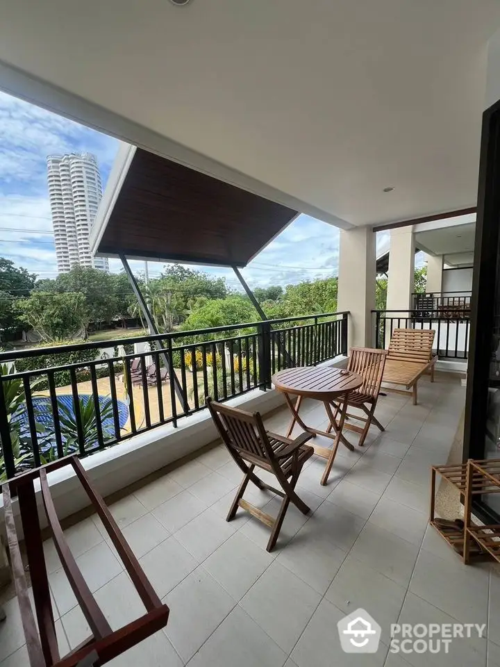 Spacious balcony with wooden furniture and scenic view of greenery and tall building.