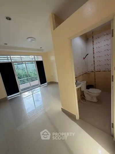 Spacious apartment with bright living area and attached bathroom, featuring large windows and modern fixtures.