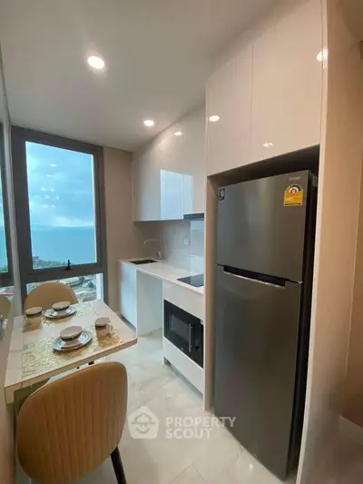 Modern kitchen with ocean view, sleek cabinets, and dining area in a high-rise apartment.