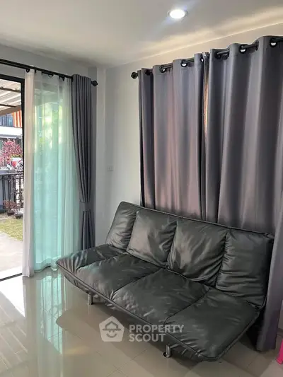 Cozy living room with modern sofa and large windows opening to a garden view, perfect for relaxation.