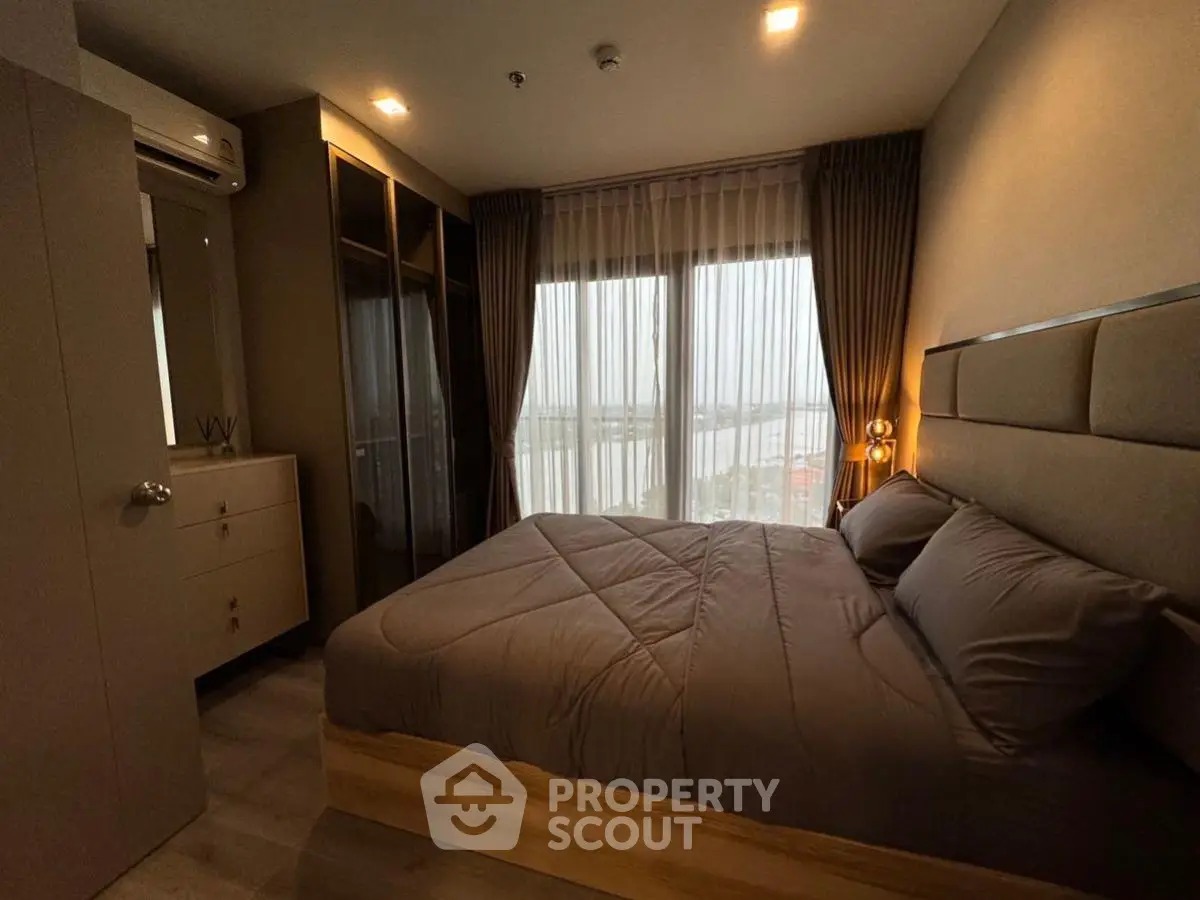 Cozy bedroom with large window offering stunning river view, modern furnishings, and ample storage space.