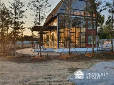 Modern glass house exterior with surrounding trees at sunset, showcasing contemporary architecture and natural beauty.