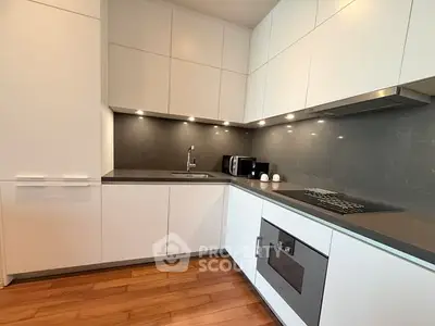 Modern kitchen with sleek white cabinets, built-in oven, and elegant wood flooring.